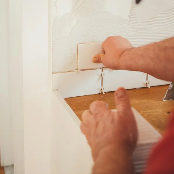 Hands setting white wall tile with spacers