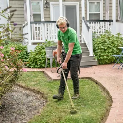 Crew lead trimming a lawn edge along a brick walkway