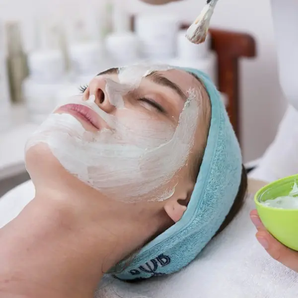 Esthetician brushing a cream mask onto a client’s face