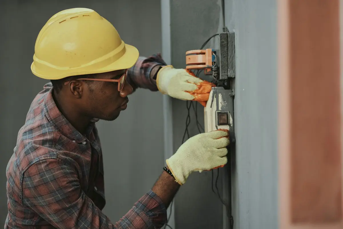 Electrician in a hard hat installing wiring at a wall box