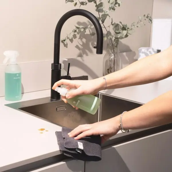 Hands wiping a kitchen counter beside the sink