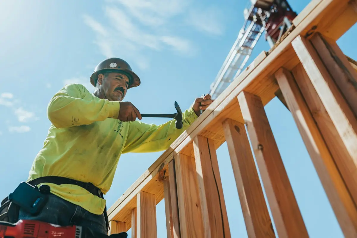 Framer hammering a wood stud wall against a blue sky