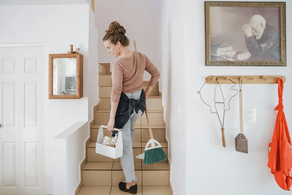 Cleaner carrying a supply caddy and broom up the stairs
