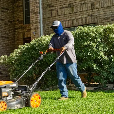 Crew member mowing a lawn beside a brick house